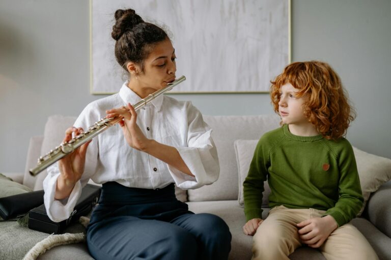 A woman teaching a child to play the flute on a sofa during a music lesson indoors.
