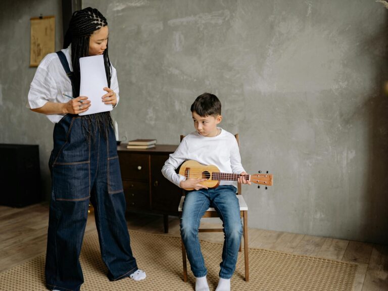 Boy with ukulele receiving instructions from teacher in a cozy classroom setting.